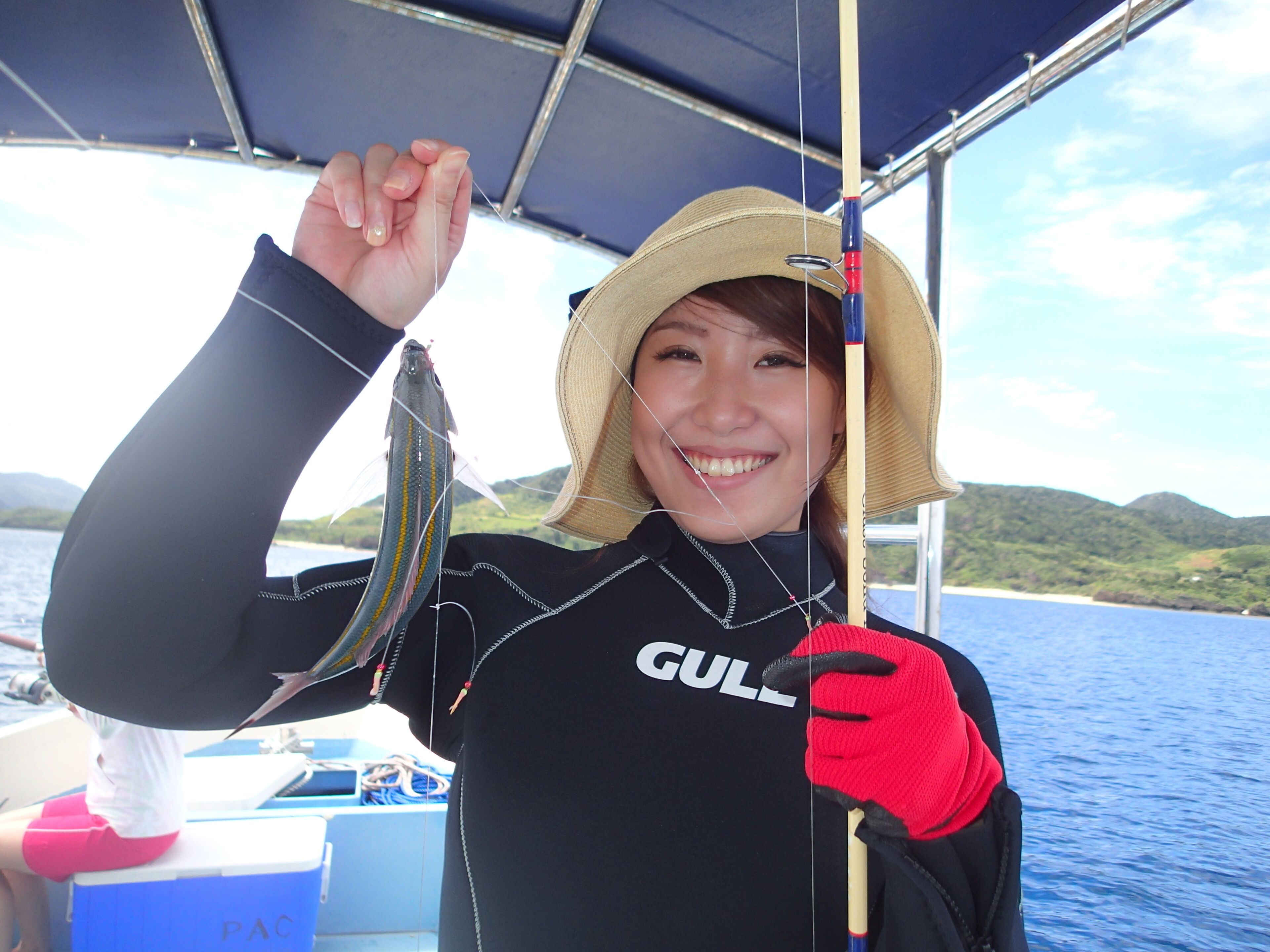 A person wearing a black wetsuit with 'GULL' on it, holding a fish.