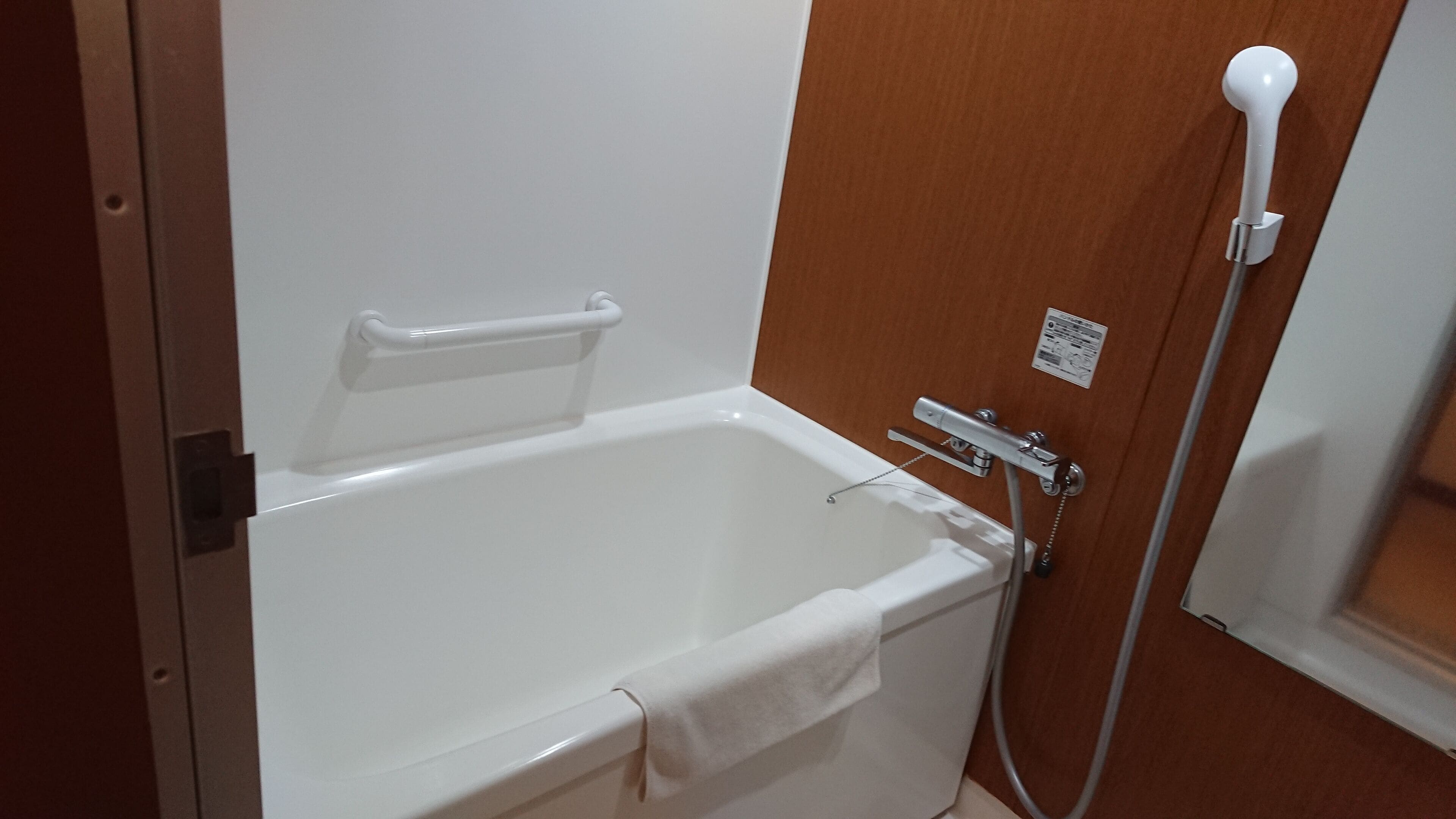 A white bathtub with a handheld showerhead and a towel.
