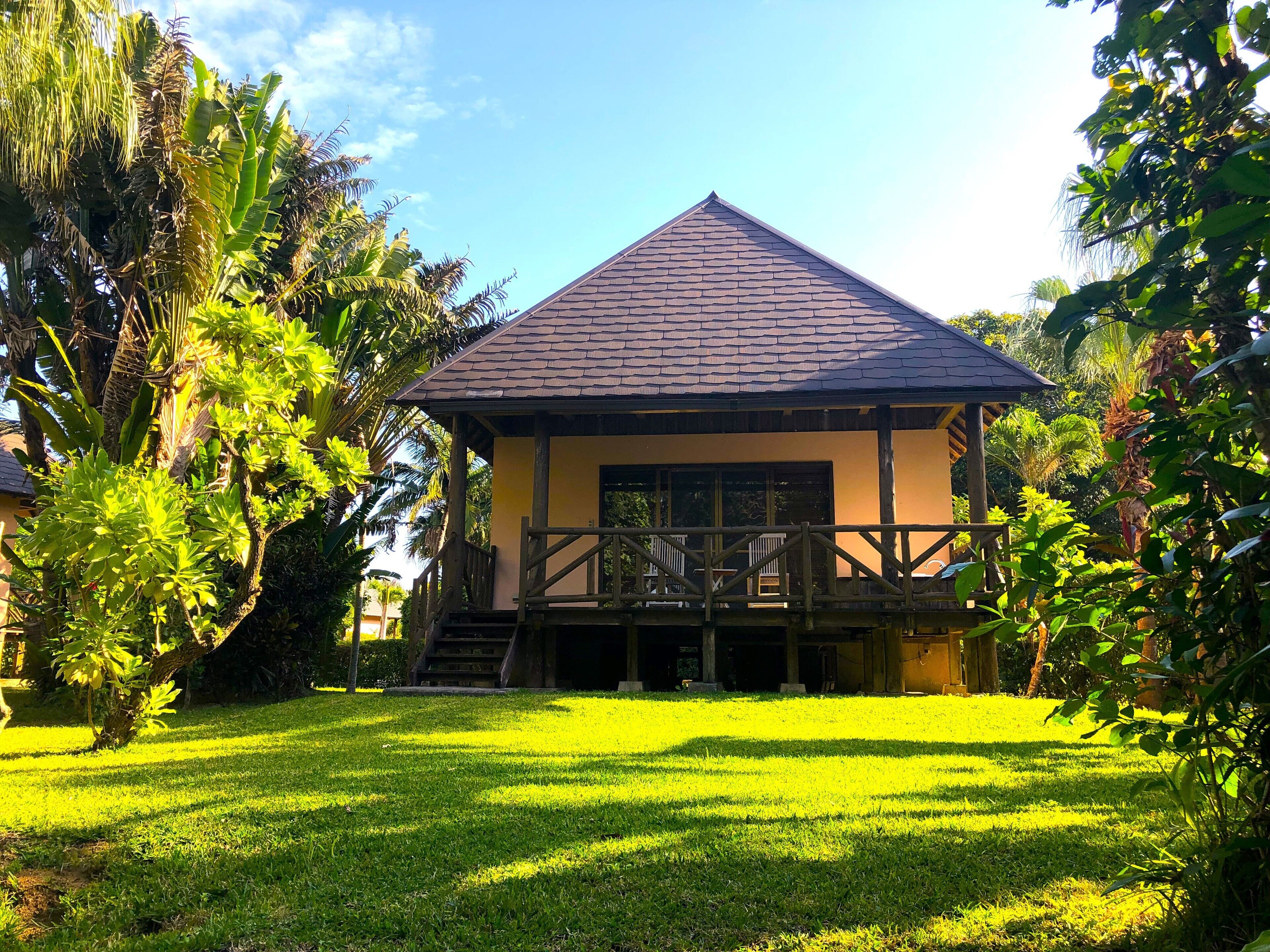A small, single-story building with a tiled roof, surrounded by lush greenery and a well-maintained lawn.