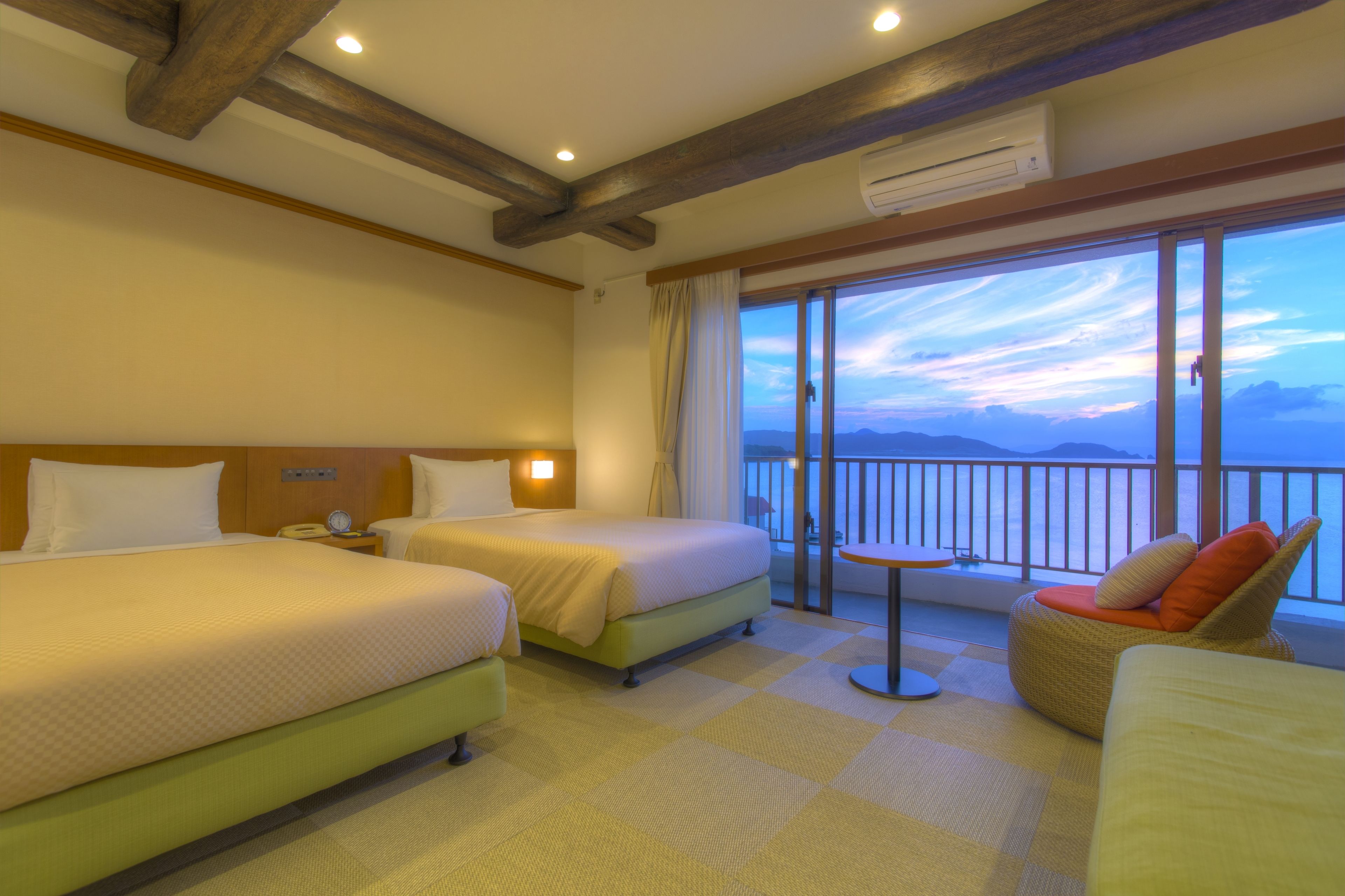 A hotel room with two beds, a balcony with a view, and a small table.