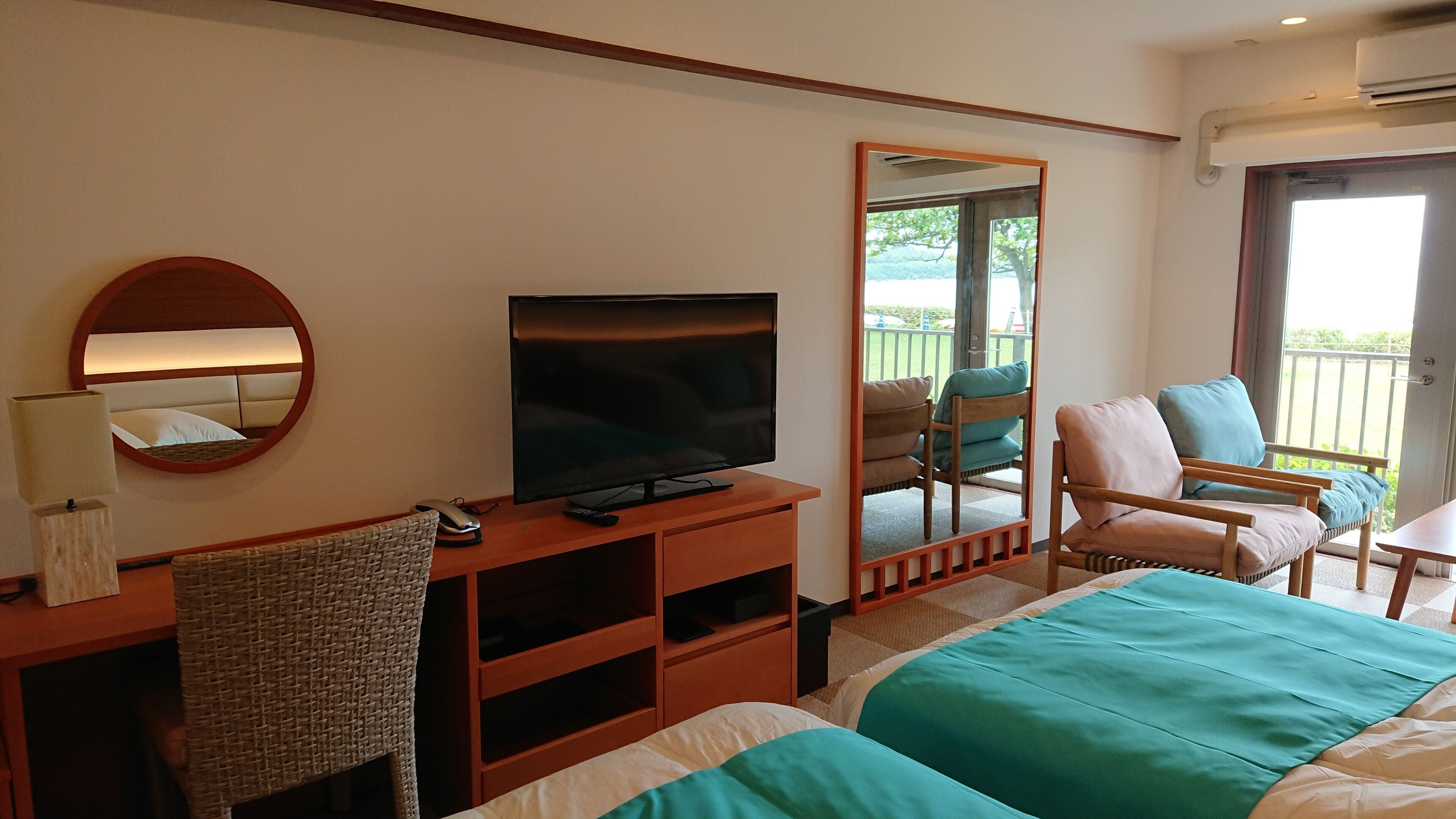 A hotel room with a bed, a TV, a desk with a lamp, a chair, and a balcony view.