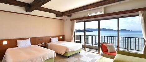 A hotel room with two beds, a balcony with a view of the sea, and a large window.