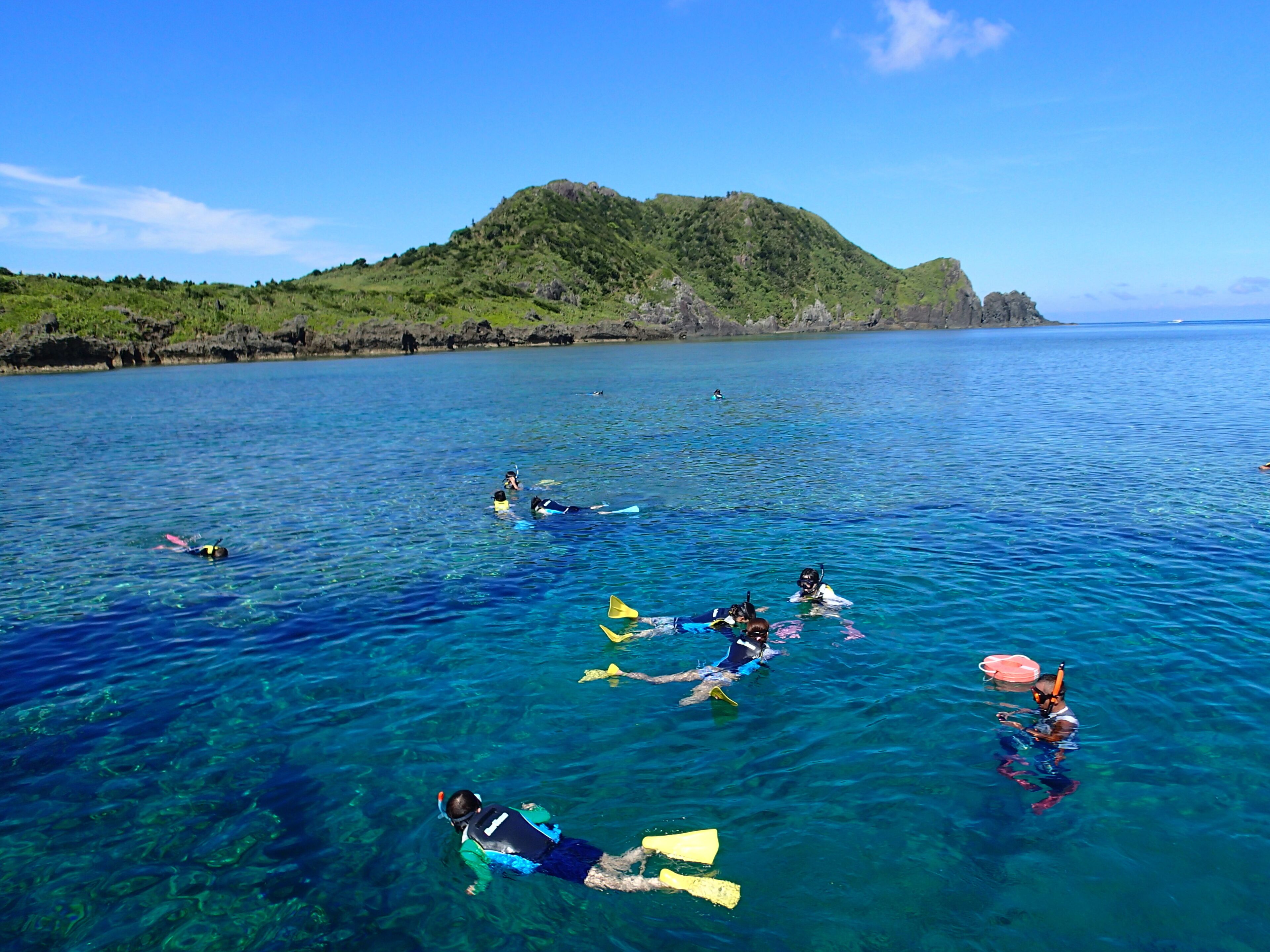 Un grupo de personas haciendo snorkel en aguas azul turquesa, con un paisaje montañoso al fondo.