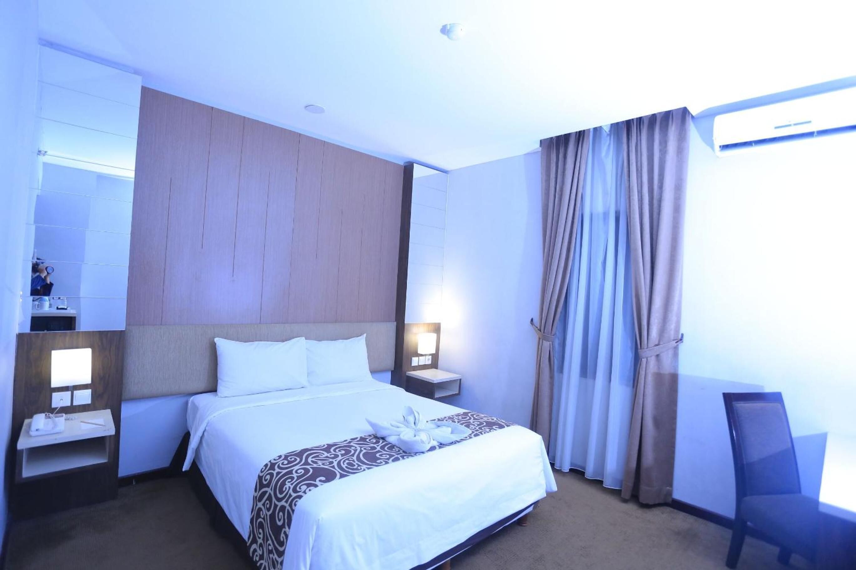 A hotel room with a large bed, two bedside tables, a nightstand, a desk, and a chair.