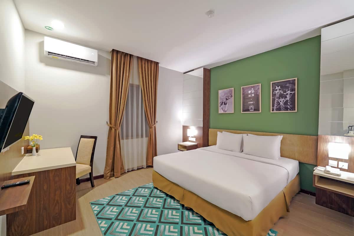 Ein Hotelzimmer mit Bett, Schreibtisch, Stuhl, Fernseher, Schreibtischlampe und einer Wand-Klimaanlage.