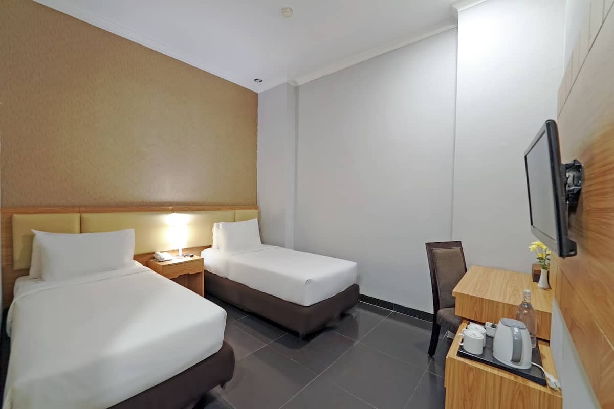 Ein Hotelzimmer mit zwei Einzelbetten, einem Nachttisch aus Holz mit Telefon und Lampe, einem Schreibtisch aus Holz mit Kaffeemaschine und einem an der Wand befestigten Fernseher.