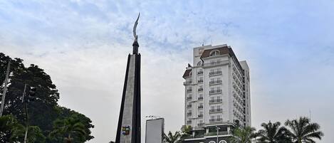 A tall monument with a spire, a white building with balconies, and palm trees in the foreground.
