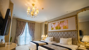 A hotel room with two beds, a chandelier, a large mirror, and a painting on the wall. - Amaroossa Royal Bogor (Bogor)