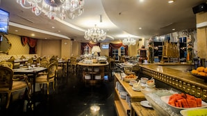 A luxurious dining area with chandeliers, round tables, and a buffet with fruits and dishes. - Amaroossa Royal Bogor (Bogor)