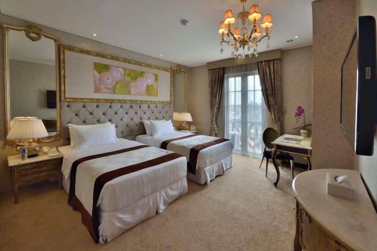 A hotel room with two beds, a large mirror, a chandelier, a desk, and a bathroom.