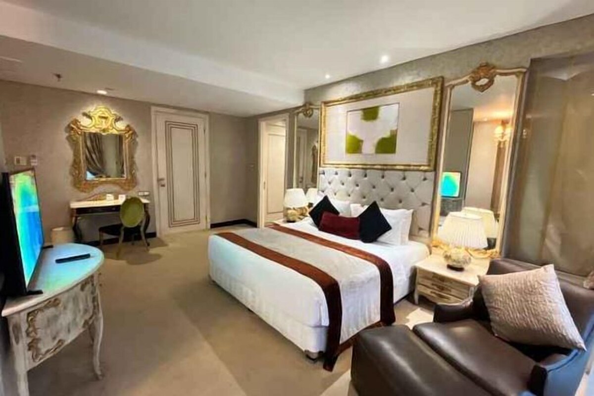 A hotel room with a large bed, a desk, a chair, a television, and a sofa.