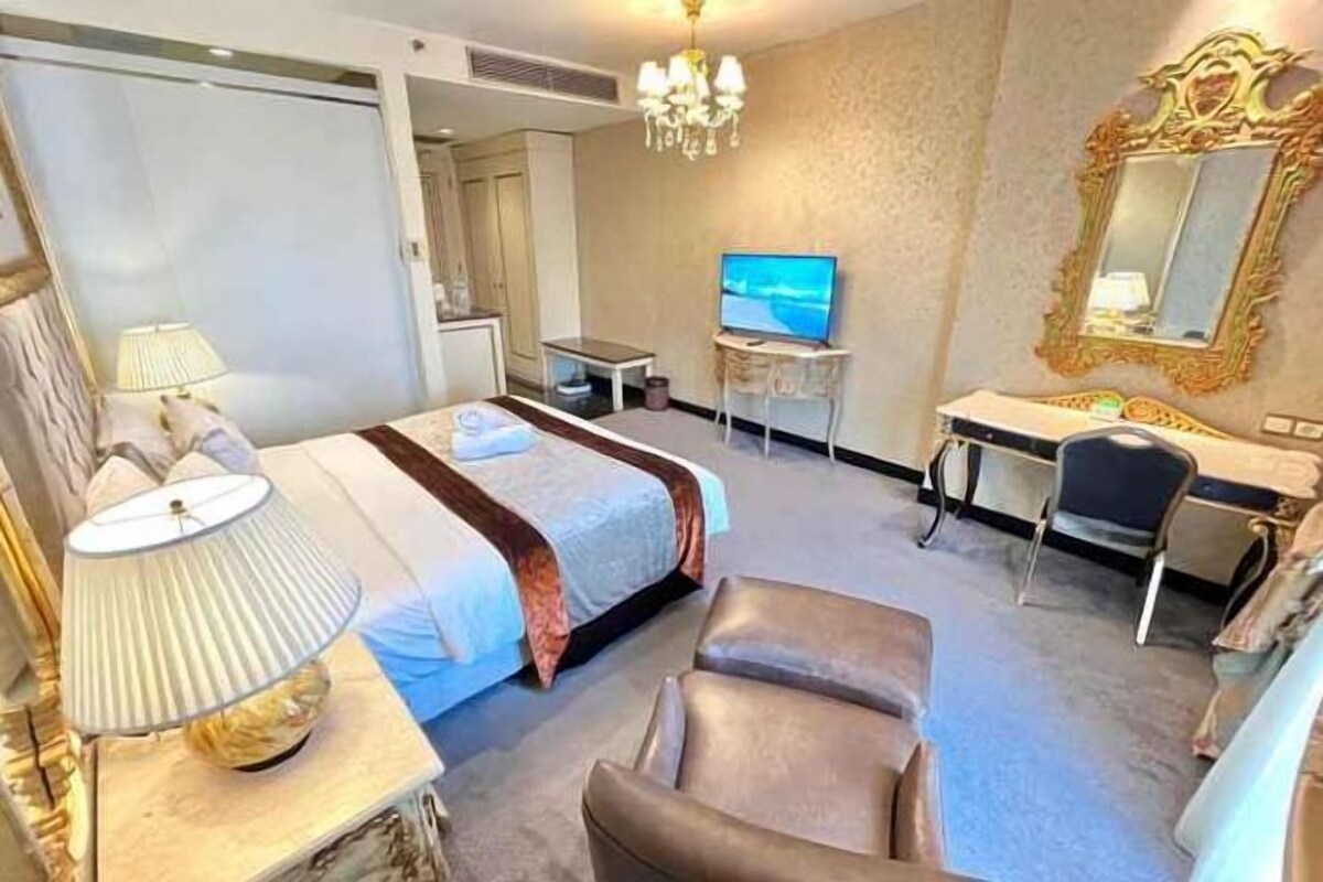 A hotel room with a bed, a desk, a chair, a television, and a mirror.