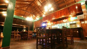 An indoor wooden bar area with tables and chairs, a counter with a display case, and a high ceiling with exposed beams. - Tabin Wildlife Resort (Lahad Datu)