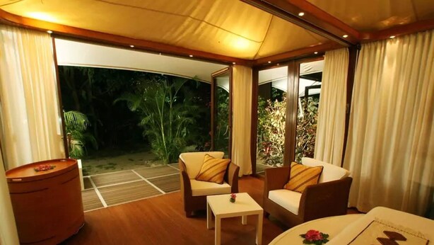Una habitación con piso de madera, dos sofás, una mesita y un ventanal con cortinas.