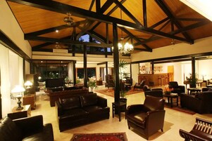 A spacious living area with a high ceiling, leather sofas, and a dining area with chairs and a table.