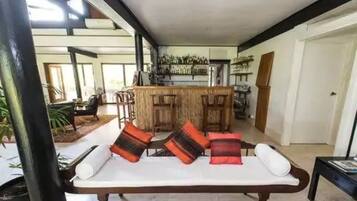 A spacious living area with a white sofa, a wooden coffee table, and a bar area in the background.