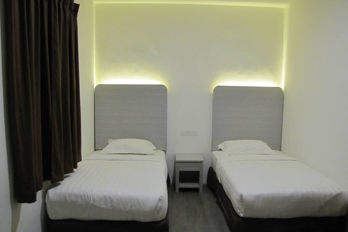 A hotel room with two single beds, a small bedside table, and a wall-mounted light fixture.