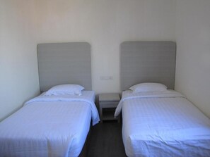 Two single beds with headboards, a nightstand, and a wall socket.