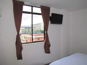 A room with a bed, a window with curtains, and a wall-mounted TV.