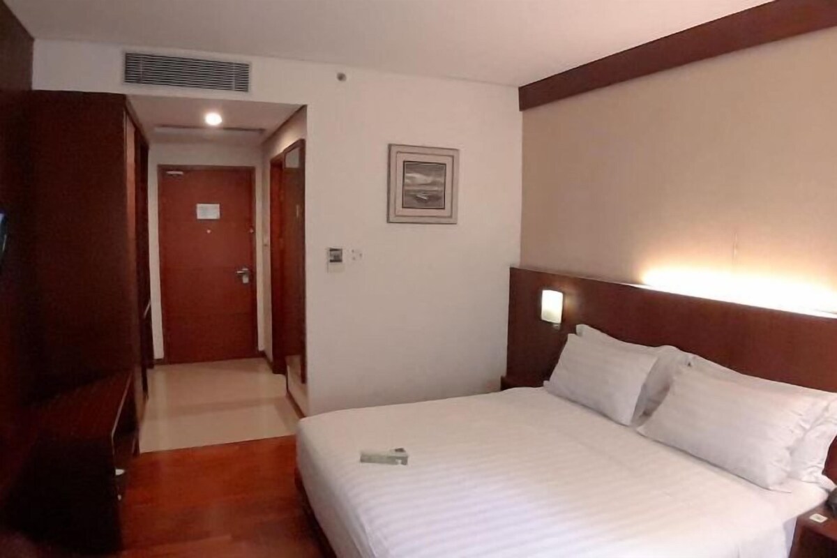 A hotel room with a bed, a nightstand, a wooden wardrobe, a door, and a framed picture on the wall.
