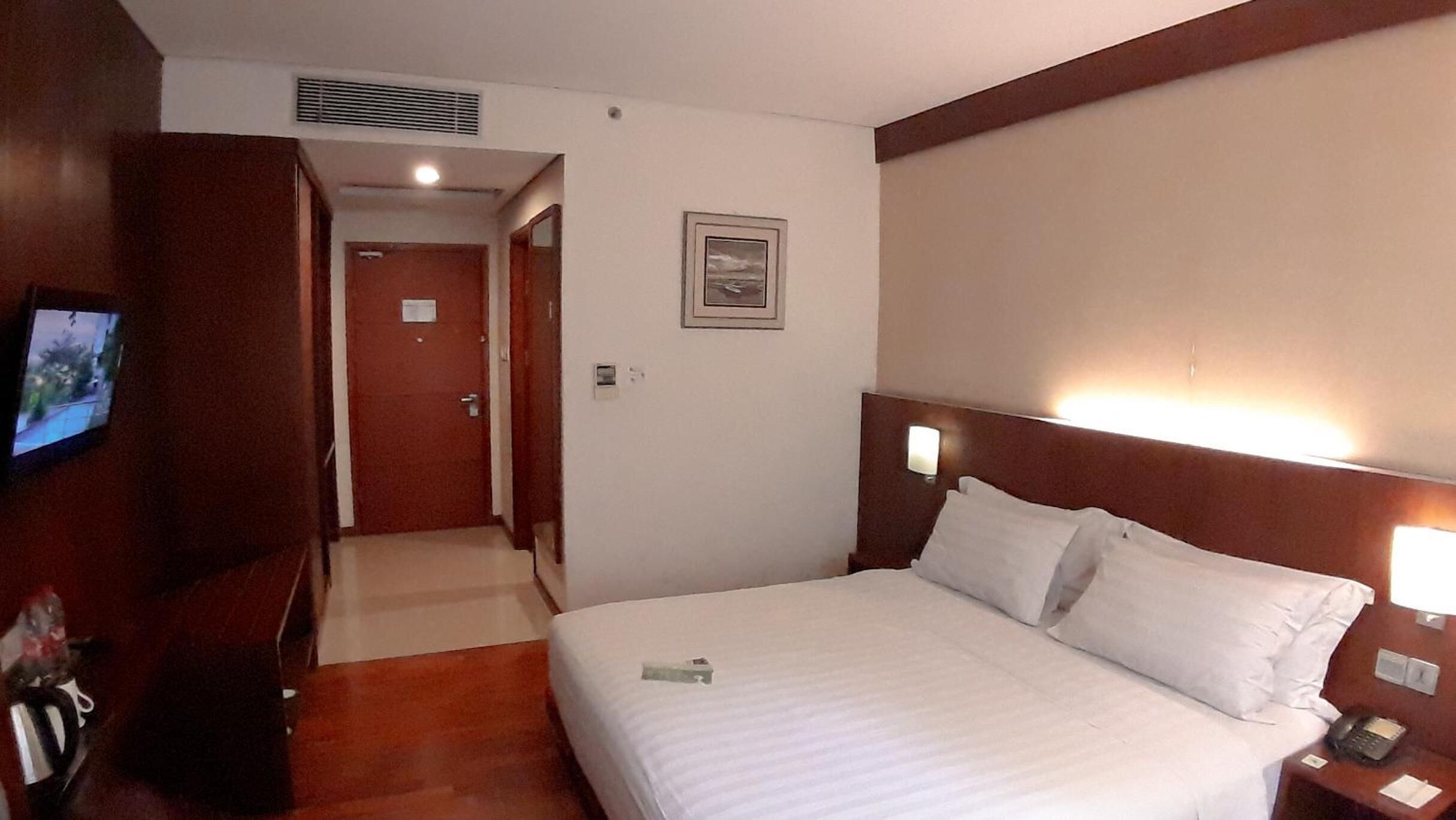Habitación de hotel con cama, mesita de noche y televisión a la izquierda.
