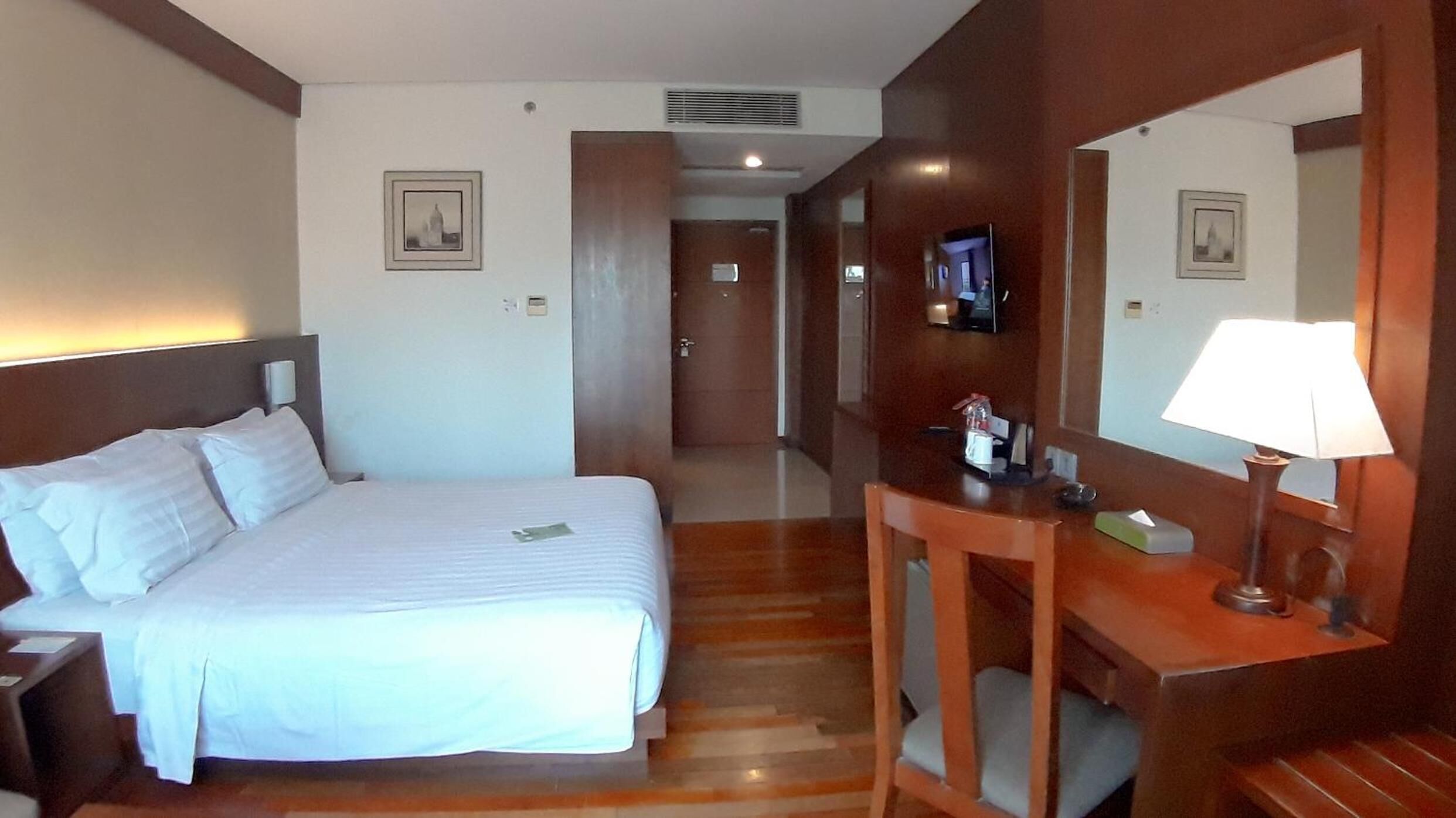 A hotel room with a bed, a desk, a chair, a mirror, and a television.