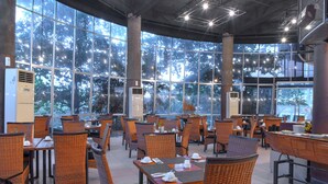 A spacious indoor dining area with wicker furniture and large windows offering a view of trees. - Oak Tree Emerald Hotel & Conventions Semarang (Semarang)