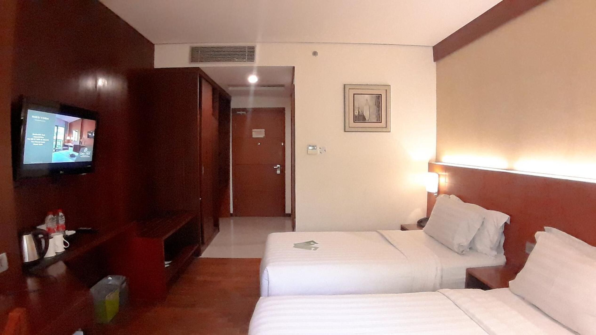 A hotel room with two beds, a TV, a desk, and a door leading to another room.