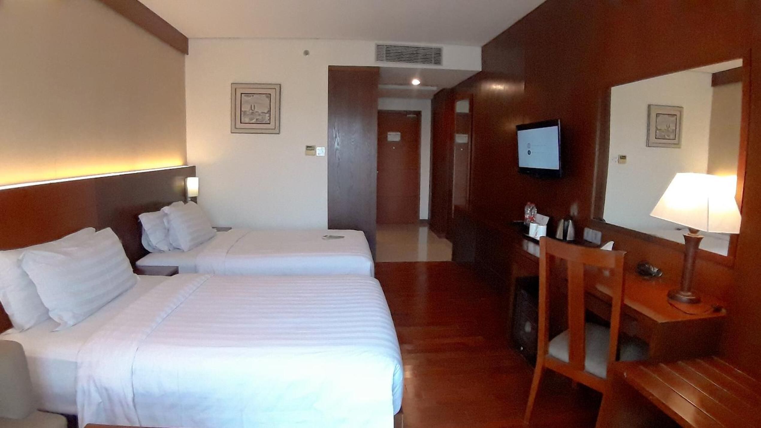 A hotel room with two beds, a desk, a chair, a TV, and a mirror.