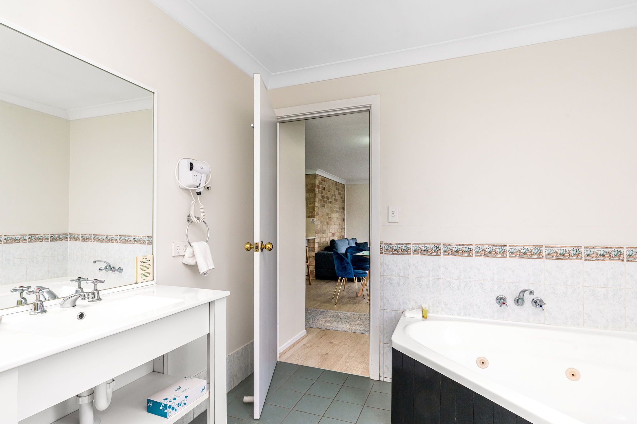 A bathroom with a white sink, a mirror, and a bathtub. There is a towel rack and a hairdryer on the wall.