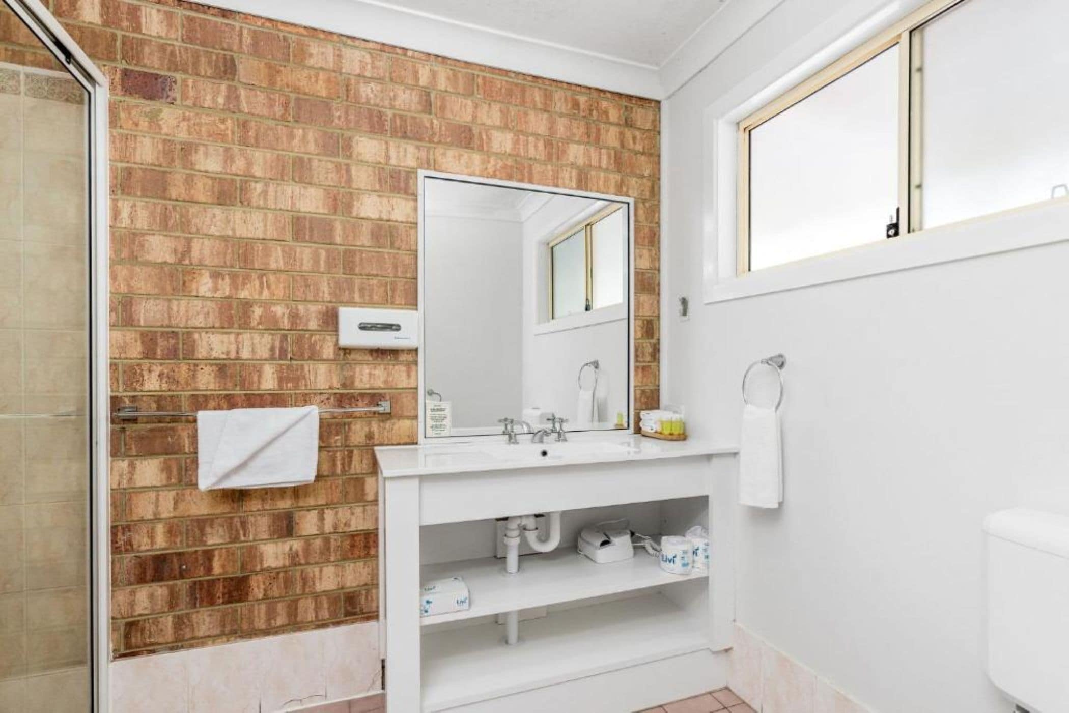 Ein Badezimmer mit Backsteinwand, Waschbecken, Spiegel und Toilette.