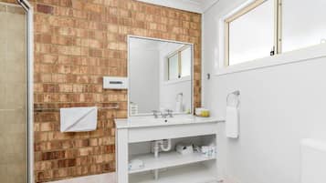 Ein Badezimmer mit Backsteinwand, Waschbecken, Spiegel und Toilette.