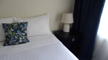 Ett hotellrum med en säng, ett nattduksbord med en lampa och ett fönster med gardiner.