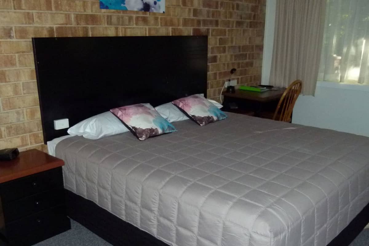 Una cama con cabecera acolchada, una mesita de noche y un escritorio con silla.