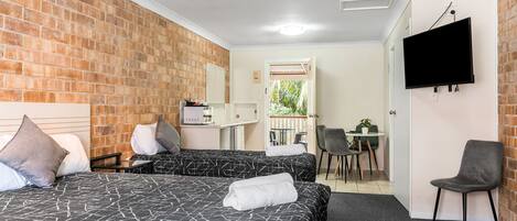 A hotel room with two beds, a TV, a desk, and a balcony with a view of greenery.