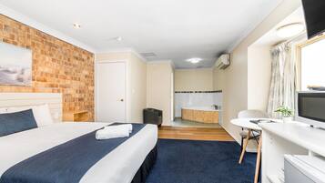 Habitación de hotel con una cama grande, un escritorio, una silla, un televisor y un baño con bañera, además de una pared de ladrillo.