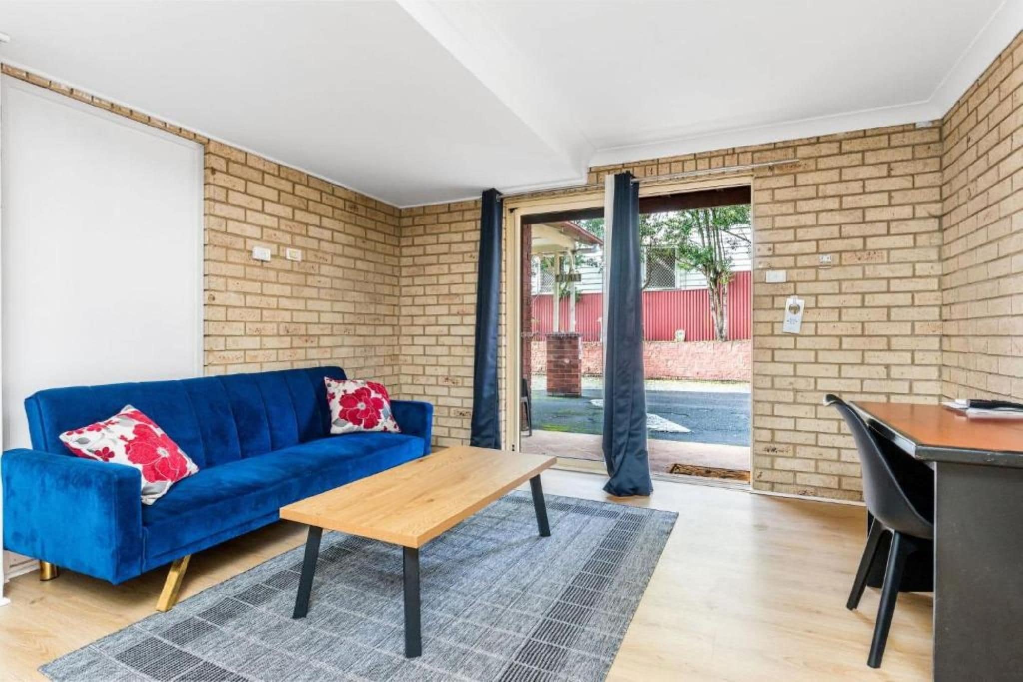 A furnished room with a blue sofa, a wooden coffee table, a black desk, and a grey rug.