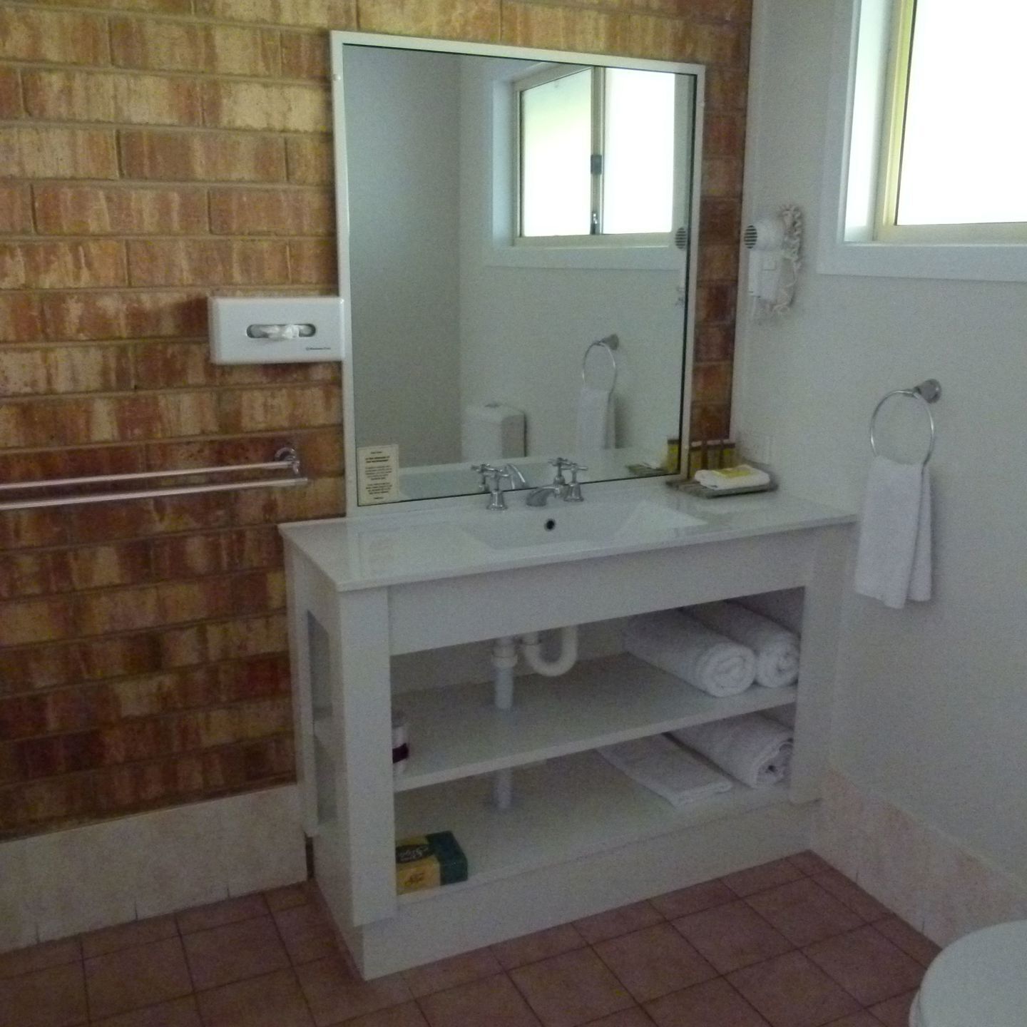 A bathroom with a white sink, a mirror, a towel rack, and a towel dispenser.