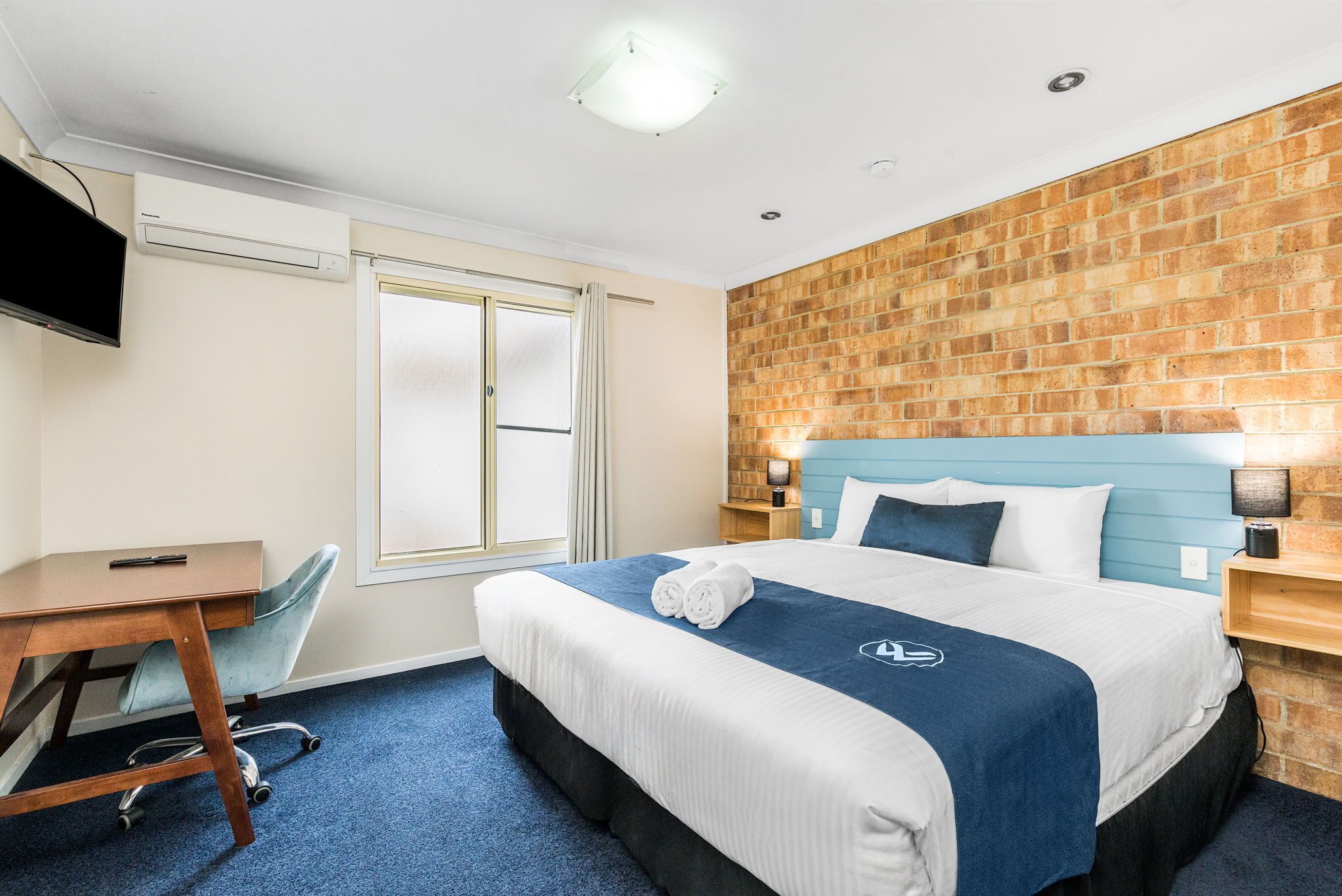 Une chambre d’hôtel avec un lit, un bureau, une chaise, une télévision et un mur en briques.