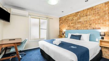 Une chambre d’hôtel avec un lit, un bureau, une chaise, une télévision et un mur en briques.