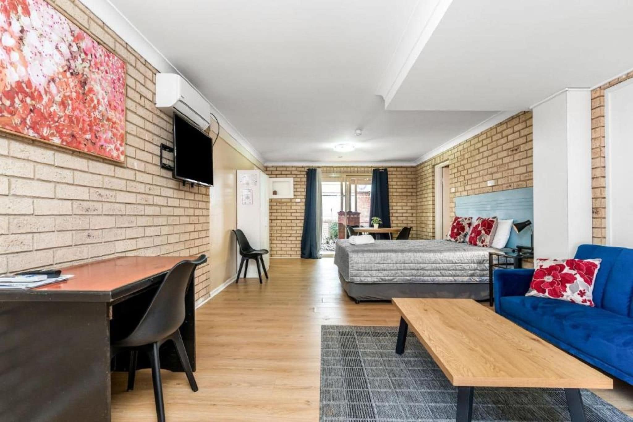 A room with a bed, a sofa, a desk, and a TV mounted on the wall.