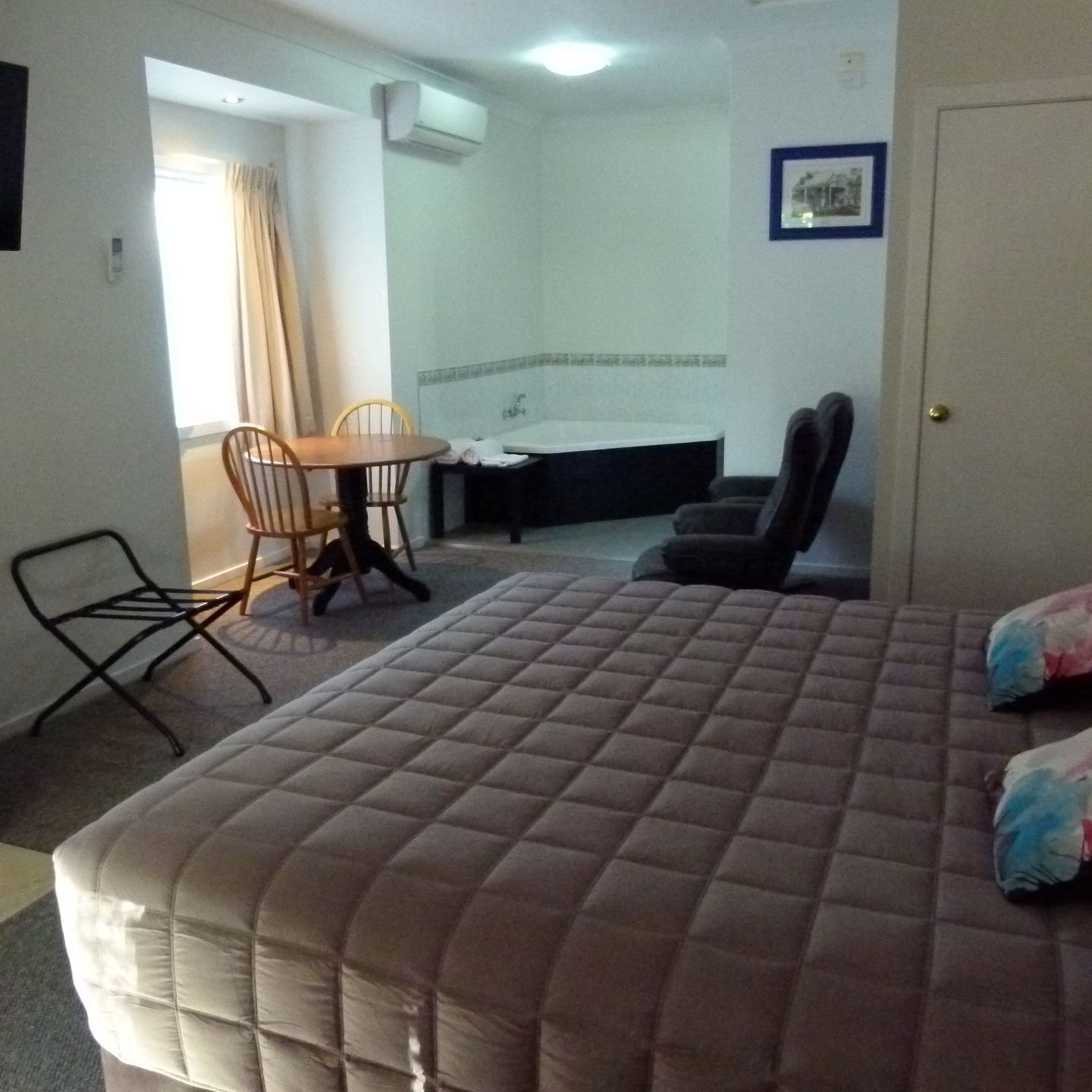 A hotel room with a bed, a chair, a table, a sink, and a shower.