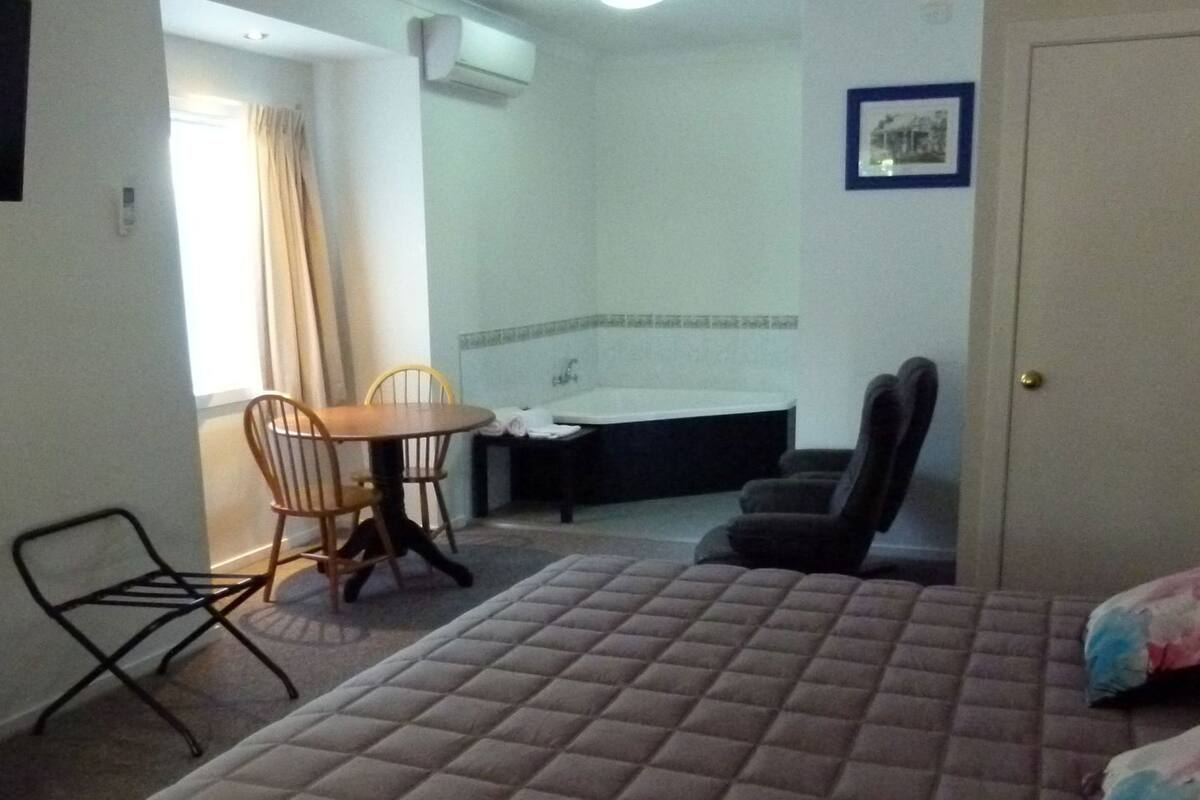 Una habitación de hotel con una cama, una silla, una mesa, un lavabo y una ducha.