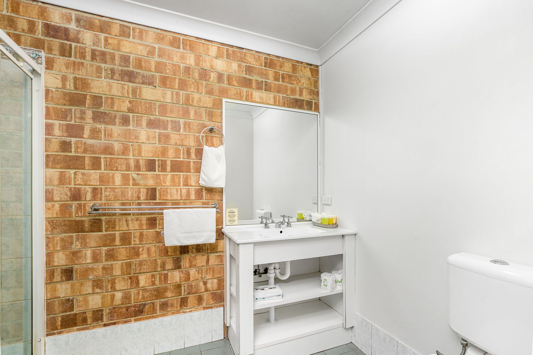 A bathroom with a brick wall, a white sink, a mirror, and a toilet.