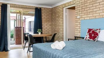 Habitación de hotel con una cama, un escritorio y una silla. Se ve una ventana con cortinas, una pared de ladrillo y un cabecero azul.