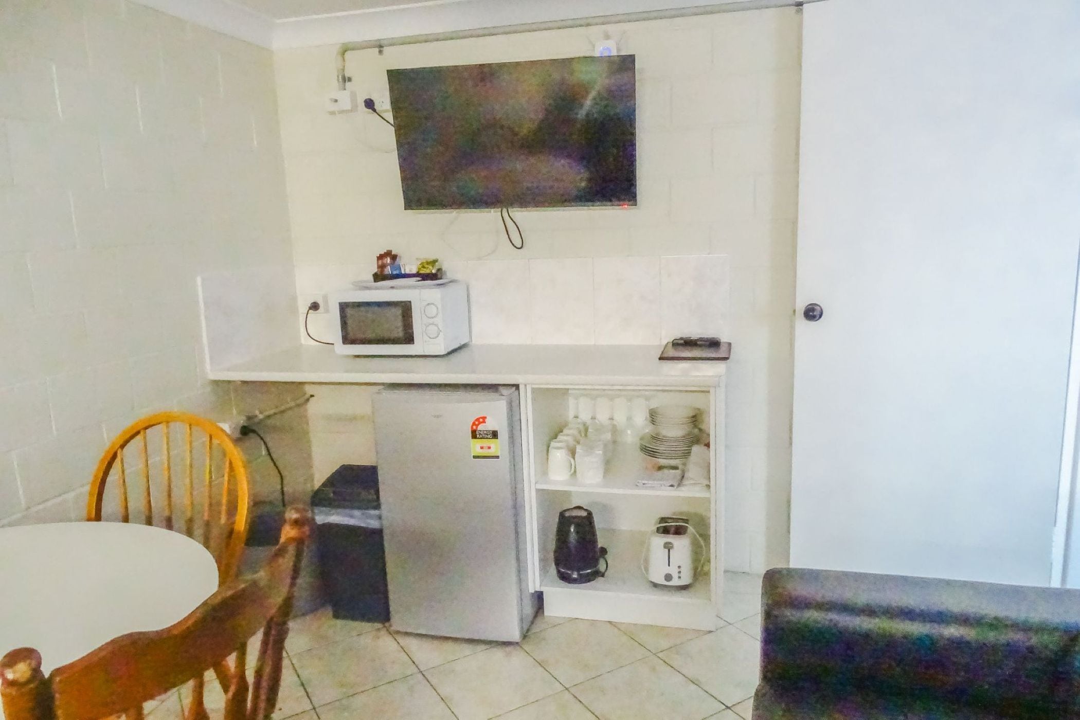 A compact kitchenette with a microwave, refrigerator, and shelves with kitchenware.