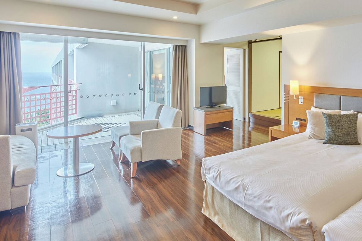 A hotel room with a large bed, a TV, a desk, a chair, and a balcony with a view.