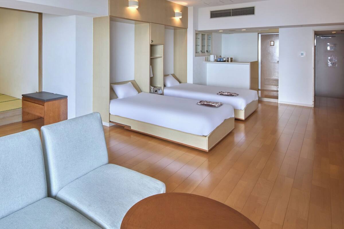 A hotel room with a sofa, a bed, a small table, a television, and a mirror.