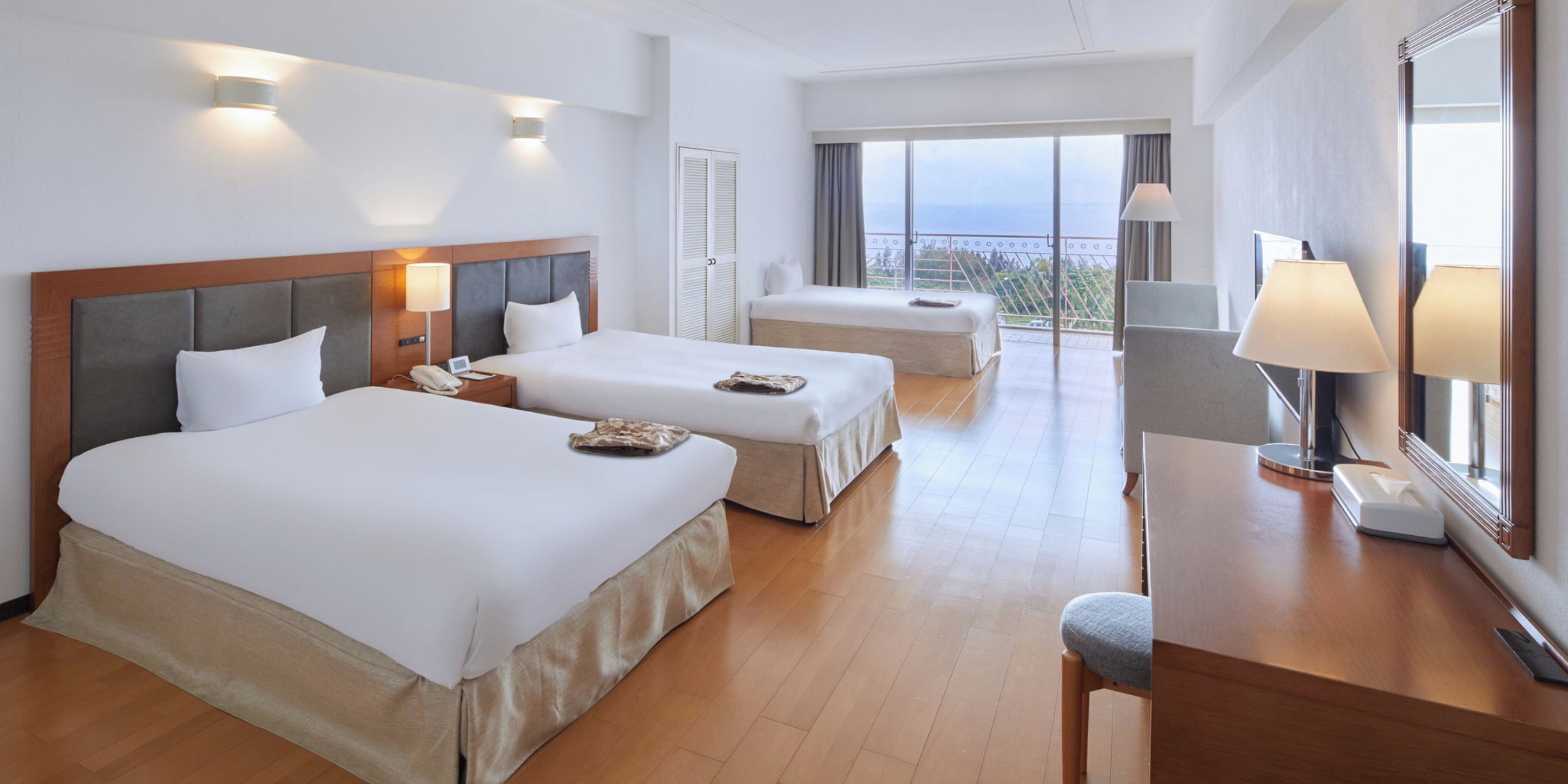A hotel room with two beds, a desk, a chair, and a large window with a view.