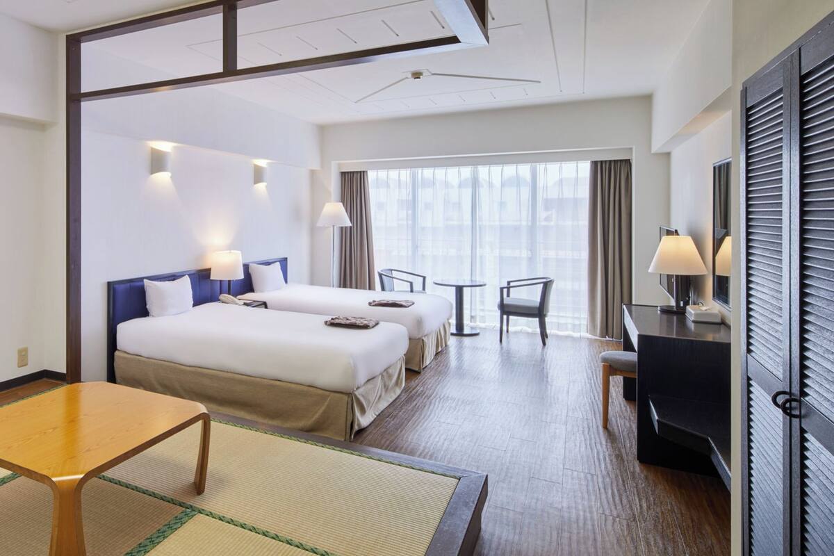 A hotel room with a bed, a desk, a chair, a TV, and a window with curtains.